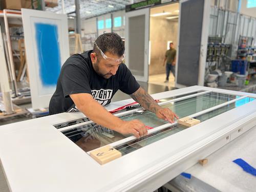 Employé de Metrie mesurant le verre d'une porte extérieure dans l'atelier de fabrication de portes
