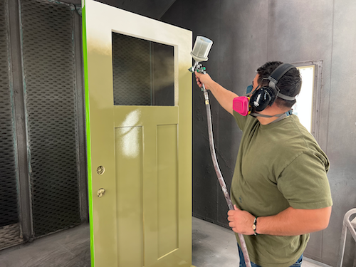 Employé de Metrie peignant une porte extérieure en vert mousse à l'aide d'un pulvérisateur de peinture