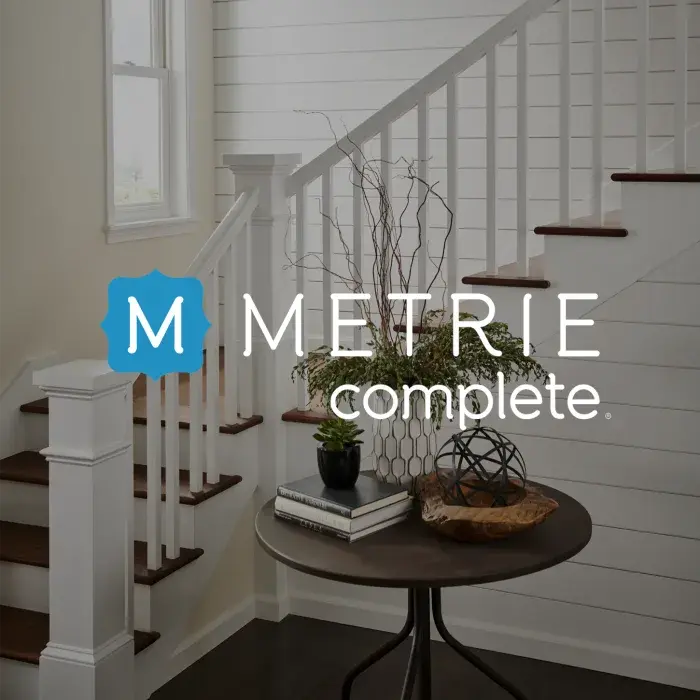 A closeup of a staircase with Metrie Complete white pre-painted shiplap. The image has a dark overlay and the Metrie Complete logo overlaid over top.
